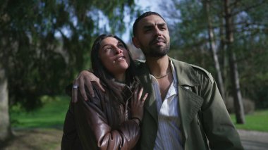 Orta Doğulu bir çift, güzel güneşli bir günde, parkın içinde gülücükler saçan ve şefkatle kucaklaşan bir şekilde geziniyorlar.