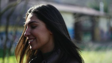 Güneş ışığı parkında tasasız bir ifadeyle yürüyen mutlu, genç bir kadın. 20 'li yaşlardaki neşeli bir kadının portresi.