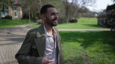 Mutlu, kendinden emin bir Arap parkın dışında yürüyüp gün ışığının ve temiz havanın tadını çıkarıyor. Orta Doğulu bir insanın gülümsemesi ve tasasız kalmasının görüntüsü.