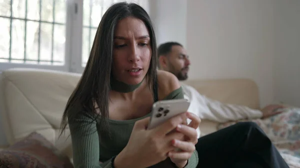 バックグラウンドで彼氏と自宅のソファに座って電話をチェック若い女性 携帯電話の画面を屋内で見ている中東の大人の女の子 — ストック写真