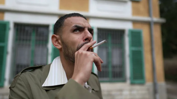 思いやりのある表情で外でタバコを吸っているある重大な中東の若者 横たわりしながら顔を撃たれた — ストック写真