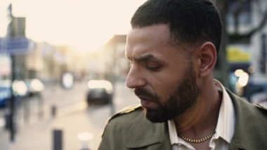 Düşünceli bir Arap genç adam ciddi bir ifadeyle şehir caddesinde duruyor. Şehir kaldırımında bir Orta Doğulu erkek.