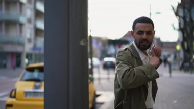 Ceket giyen neşeli bir Orta Doğulu adam, bir şehir caddesinde kameraya doğru yürüyor ve başarısını mutlulukla kutluyor.