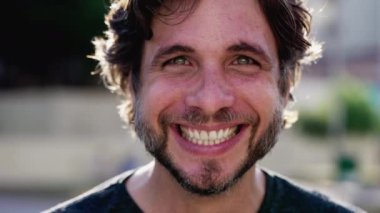 Neşeli bir adamın portresi büyük bir gülümsemeyle dışarıda güneş ışığında duruyor. 30 'lu yaşlarda bir erkek kameraya bakıyor.