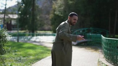 Neşeli bir adam, neşe ve coşkuyla dolu güneşli bir parkta başarıyı kutluyor.