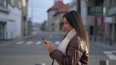 Şehir caddesinde duran cep telefonu cihazına bakan genç bir kadın. 20 'li yaşlarda bir kızın ekrana bakarken ki hareketli görüntüsü.