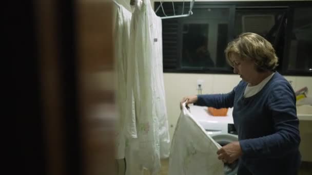 洗濯室のラックで乾燥させるためにシートを置くことができますシニア女性 服を乾かす者 — ストック動画