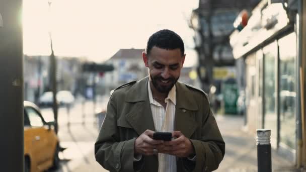 Joven Feliz Oriente Medio Caminando Calle Ciudad Sosteniendo Dispositivo Teléfono — Vídeo de stock