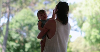 Anne, arka bahçede oğluyla etkileşime giriyor. Ebeveyn kucağında bebeğin silueti