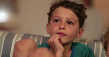 Çocuk suratlı, geceleri kanepede televizyon seyrediyor.