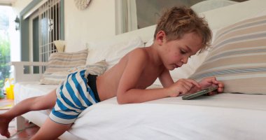 Casual little boy child using cellphone lying on sofa