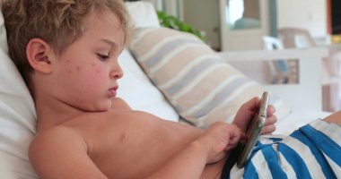 Child toddler holding smartphone lying at home sofa