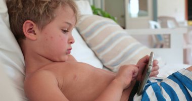 Child toddler holding smartphone lying at home sofa
