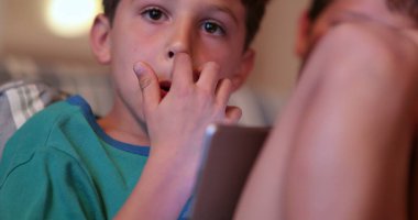 Evdeki gizli çocuk elinde tablet cihazıyla ekrana bakıyor. Teknoloji kullanan gizli çocuklar.