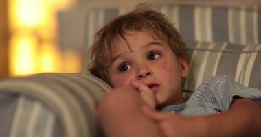 Cute toddler infant boy at couch in the evening watching TV