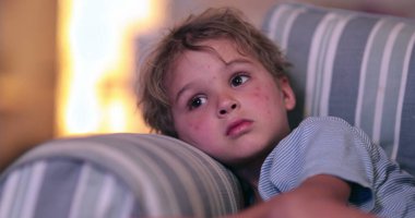 Child boy watching TV at night on couch. Candid kid staring at screen real expression reactions