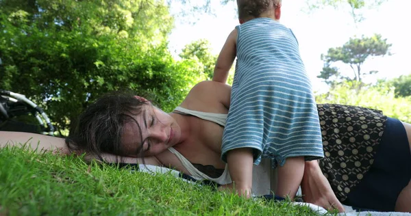 外の草の上で寝ている母 疲れ果てた親は屋外で休んで 赤ちゃんは注目したい — ストック写真