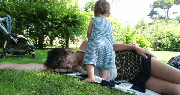 母は草の上で昼寝をし 母の注意を望んでいる赤ん坊は 睡眠から目覚める — ストック写真