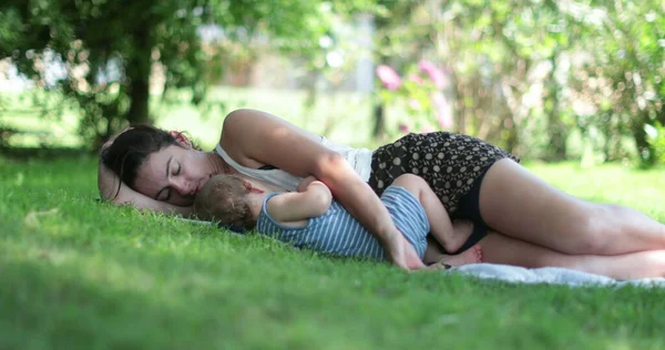 Mom resting with baby laid on grass outside