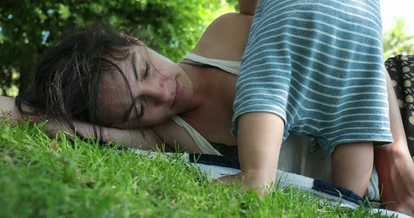 疲れて母親は外で草の上に寝そべって 赤ちゃんは注目したい 昼寝から親を目覚めさせる — ストック写真