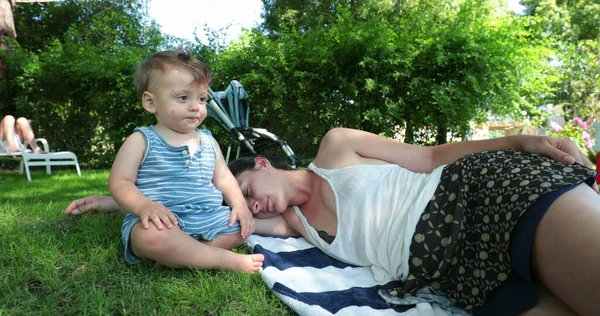 疲れた母は赤ん坊の赤ん坊の隣で寝ている外の草の上に横たわっていた — ストック写真