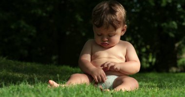 Cute baby seated outdoors in nature. Infant toddler boy learning about the world by touch