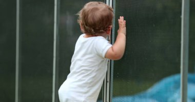 Cute baby infant leaning on swimming pool fence protection