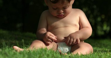 Cute baby chubby toddler infant in outdoor backyard observing own body