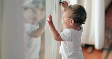 Bebek pencerenin önünde durup gitmek istiyor. Cama yaslanmış şirin bebek bebek.