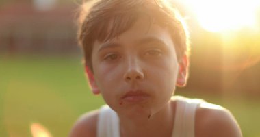 Gün batımı zaman portresi çekilirken kameraya bakan ciddi çocuk yüzü.