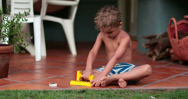 Creative child playing with building blocks outside in summer day. Toddler plays by himself