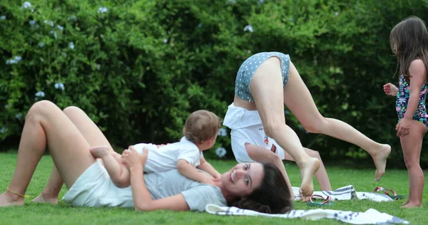 外の芝生で子供と赤ちゃんとヨガの練習をしている母親 — ストック写真