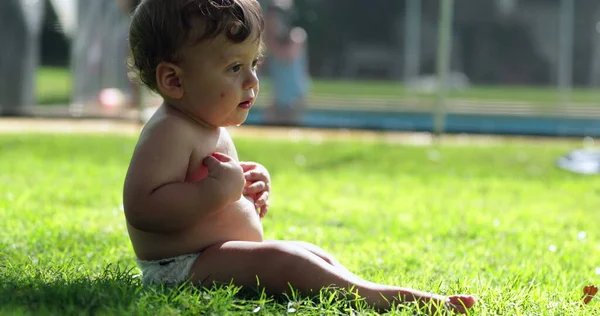Adorable infant baby in outdoor backyard grass observing own body. Cute toddler boy
