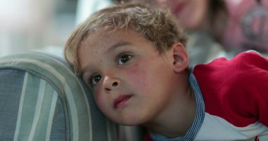 Küçük çocuk TV ekranına bakıyor hipnotize olmuş. Çocuk yatmadan önce kanepede televizyon izliyor.