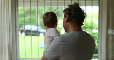 Grandparent holding grandson baby next to window during summer day