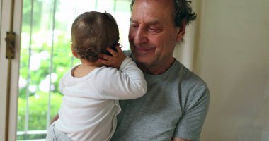 Grandfather holding baby grandson at home