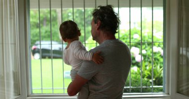 Baby and grandfather next to window during rainy day