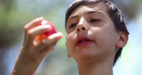 若い男の子は外で健康的な桃の実を一口飲んでいます 子供の健康的な食事 — ストック写真