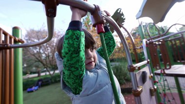 Çocuk parkında oynayan aktif küçük bir çocuk. Beyaz erkek çocuk dışarıda idman yapıyor. Metal çubuğu tutuyor.