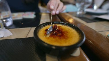 Yakından gelen el kaşıkla creme brulee yüzeyi kırıyor. Geleneksel Fransız tatlısını yiyen kişi.