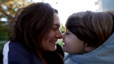 Anne ve çocuk Eskimo öpücüğü yapıyor. Anne ve oğul sevgi ve sevgi dolu bir ilişki güneşli bir günde gün ışığıyla dışarıda dikiliyor.