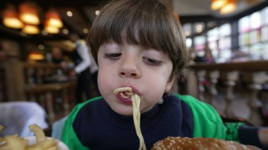 Çocuk restoranda oturmuş makarna yiyor. Erişte çiğneyen erkek çocuğun portresi. Delikanlı ağzı dolu