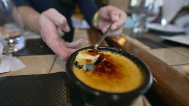 Yakından gelen el kaşıkla creme brulee yüzeyi kırıyor. Geleneksel Fransız tatlısını yiyen kişi.