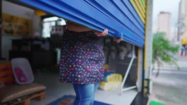 Yerel Mağazanın Kadın İşletme Sahibi garaj önü açıyor. Güne önlük giyen genç girişimci kadın başlıyor.