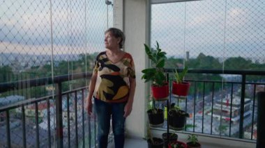 Düşünceli, son sınıf öğrencisi bir kadın apartman balkonunda dikilip, düşünceli bir ifadeyle şehir manzarasına bakıyor. Evdeki yaşlılara ait özgün günlük olay yeri