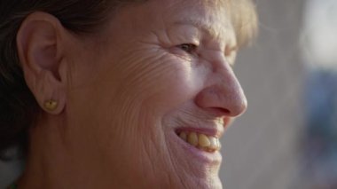 Neşeli ve dalgın gülümseyen mutlu bir son sınıf kadınının profilini çıkar. 70 'li yaşlarda mutlu bir insan pencereden dışarı bakıyor.