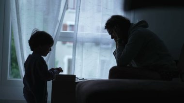 Evde eğitim gören bir çocuk siluetinde, pencerenin kenarında. Ebeveyn oğluyla oyun oynar. Çocukluk gelişimi kavramı