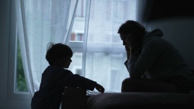 Evde eğitim gören bir çocuk siluetinde, pencerenin kenarında. Ebeveyn oğluyla oyun oynar. Çocukluk gelişimi kavramı