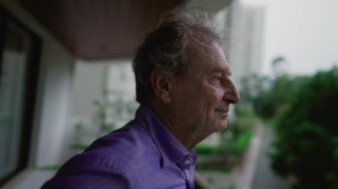 Gece vakti apartmanın balkonunda durup dışarıyı seyreden düşünceli yaşlı adam. 70 'li yaşlarda gülen ve gülümseyen yaşlı bir adamın düşünceli ifadesi.