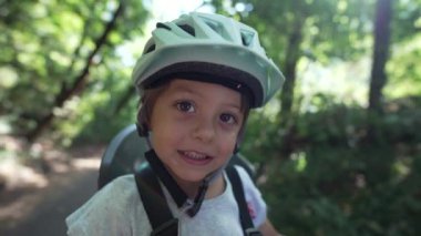 Orman parkında bisiklet kaskı takan mutlu bir çocuk. Bisikletin arkasında oturmuş gülümseyen küçük çocuk hafta sonu aktivitesi yakın plan portresi. Güvenlik ve koruma kavramı